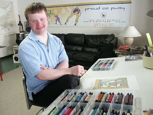 Erik, smiling and sitting at a table full of art supplies